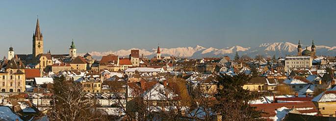 La diversit religieuse  Sibiu, figure par ses clochers. Coup dil vers le sud-est ; dans la ville enneige, lon distingue, de g.  dr. : la Tour du Conseil (difice civil, sorte de beffroi) ; le robuste clocher gothique de lglise vanglique ; le campanile (surmont dun bulbe) de lglise catholique, dite glise des Jsuites ; le clocher (coiff dune flche rouge) de lglise rforme ; enfin, un peu  lcart  droite, les deux tours et la coupole de la cathdrale orthodoxe. Dans le lointain, cimes neigeuses des Carpates mridionales.